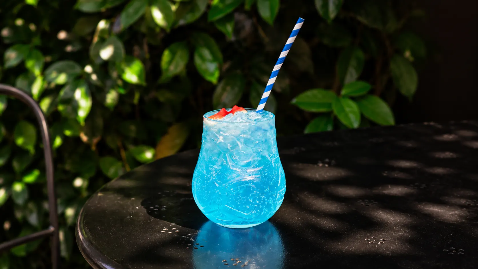 Um Blue Lagoon azul num copo trabalhado, com gelo picado e uma palhinha às riscas azuis.