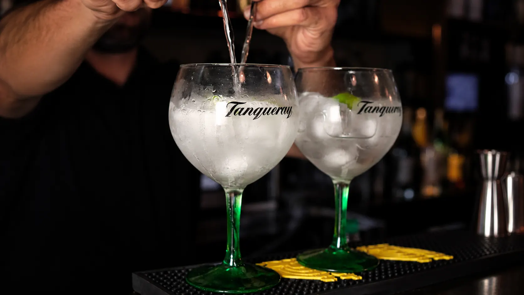 Um gin tónico a ser servido em copos balão com o nome Tanqueray gravado.