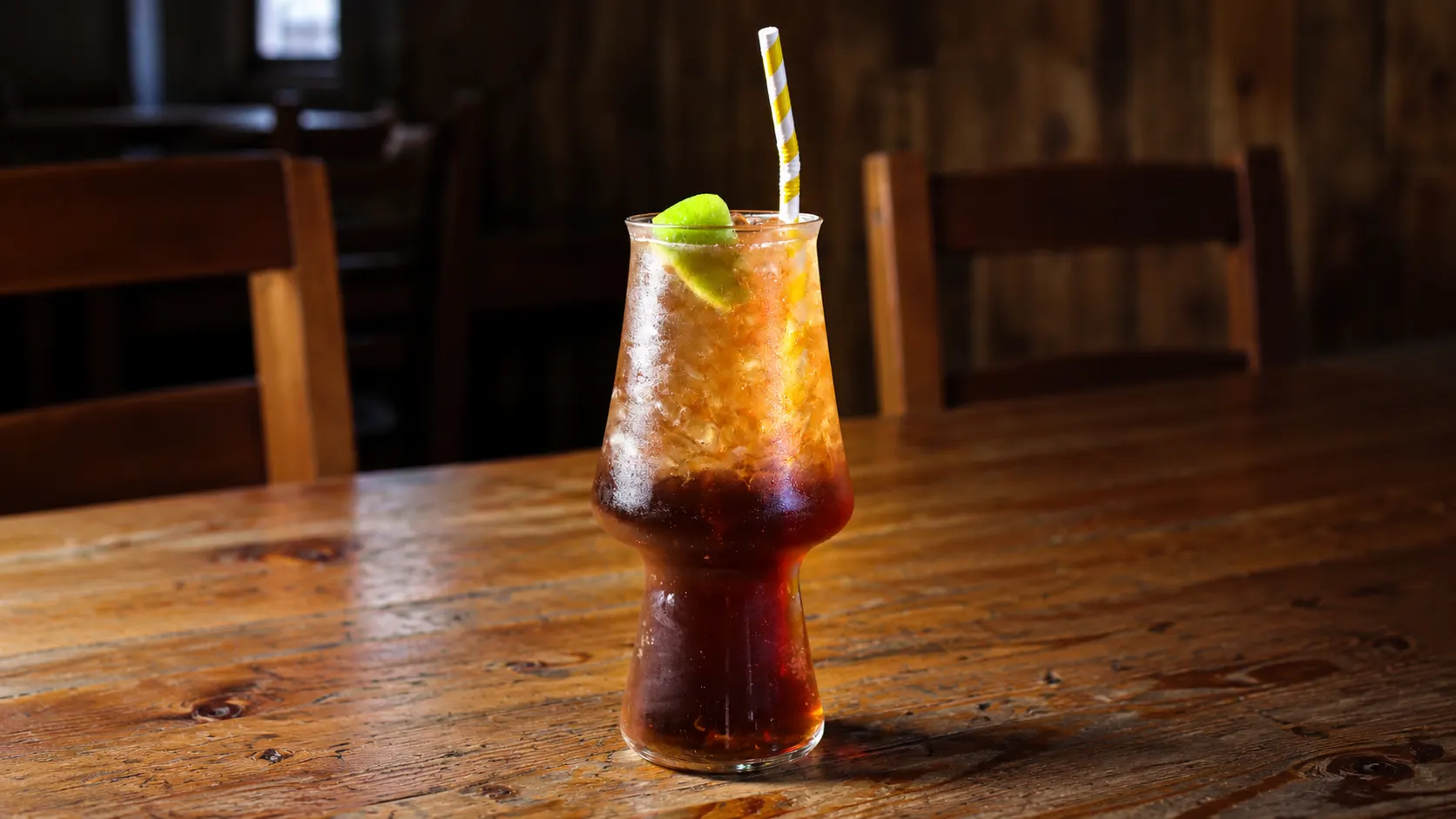 Um Long Island Iced Tea num copo alto, cor de cola, com gelo e uma rodela de lima.